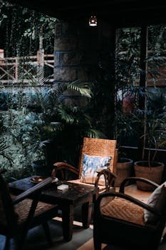 Serene patio featuring wicker chairs, table, and lush plants under ambient lighting.